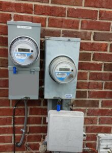 Two electric meters are attached to a brick wall.
