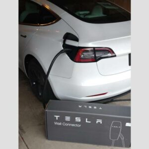 A white tesla charging in the driveway of a home.