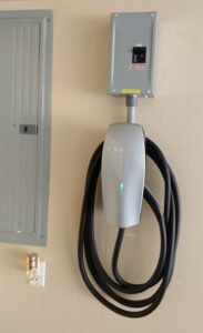 A wall mounted electric car charger with the plug plugged in.